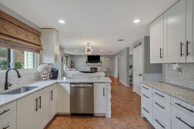 kitchen with light stone countertops, white cabinetry, a sink, stainless steel dishwasher, and open floor plan