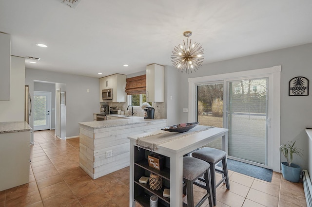 kitchen with a sink, backsplash, appliances with stainless steel finishes, white cabinets, and light tile patterned floors