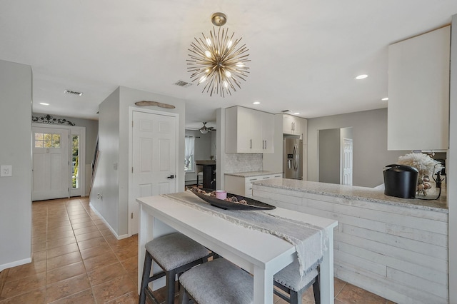 kitchen with visible vents, white cabinetry, stainless steel fridge, light countertops, and decorative backsplash