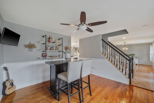 dining area with stairs, a bar, ceiling fan with notable chandelier, and light wood finished floors