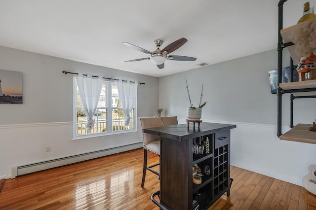 office space featuring a ceiling fan, visible vents, wood-type flooring, and a baseboard radiator