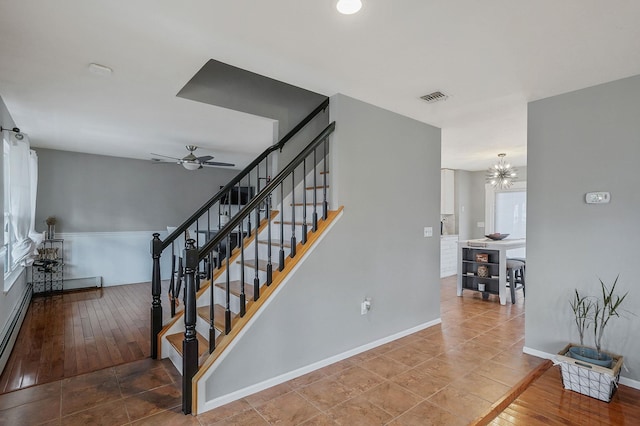 stairs with ceiling fan with notable chandelier, wood finished floors, baseboards, and visible vents