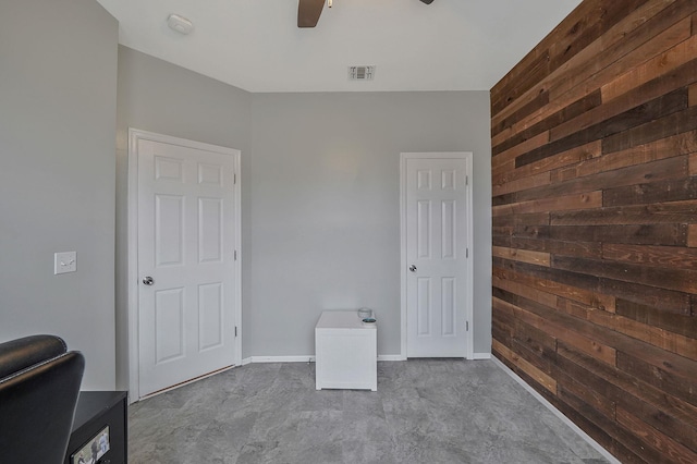 unfurnished bedroom featuring visible vents, a ceiling fan, wooden walls, baseboards, and an accent wall