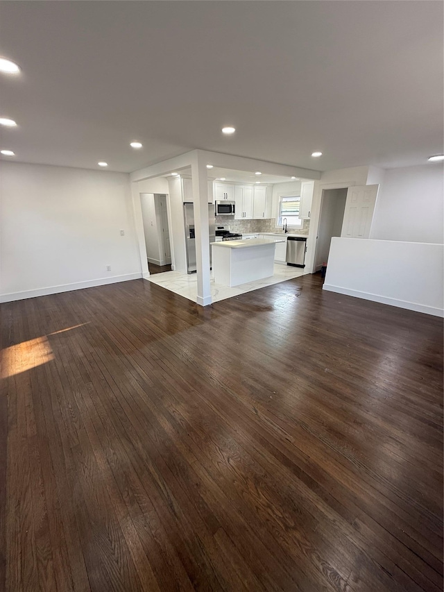 unfurnished living room featuring recessed lighting, baseboards, dark wood-type flooring, and a sink