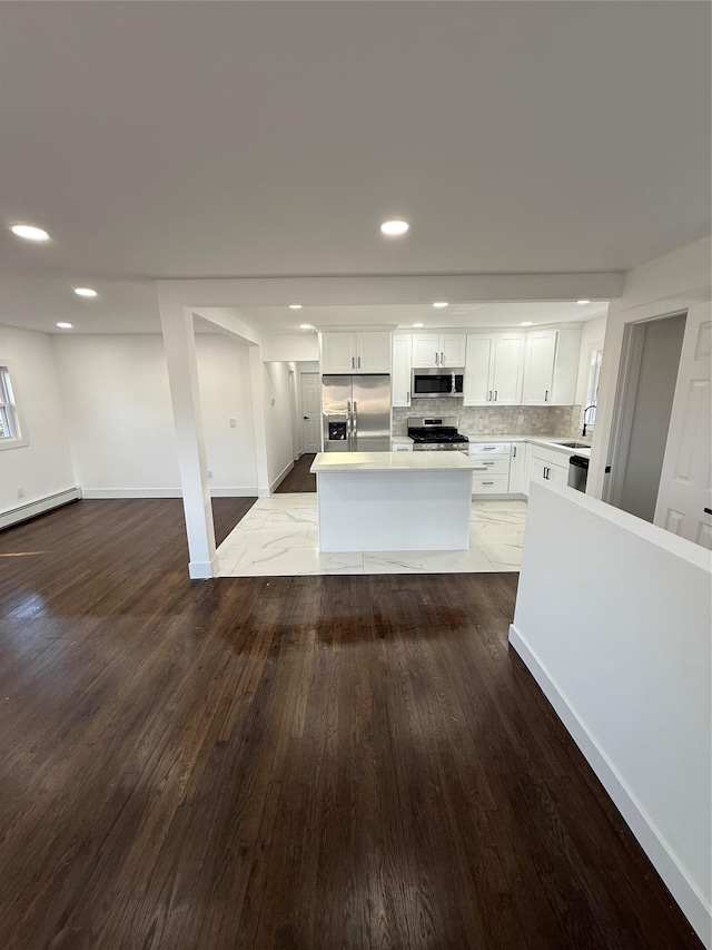 kitchen featuring wood finished floors, a center island, white cabinetry, stainless steel appliances, and decorative backsplash