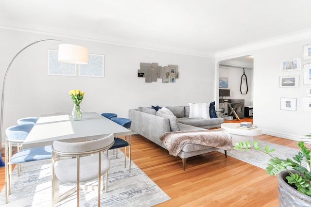 living room featuring arched walkways, light wood-style flooring, and crown molding