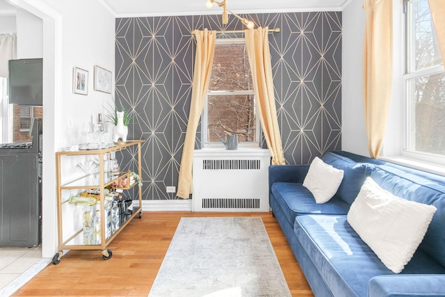 living area with an accent wall, wood finished floors, radiator heating unit, and wallpapered walls