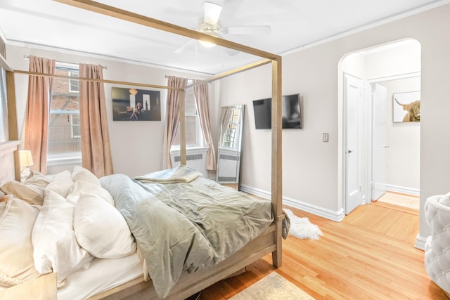 bedroom featuring wood finished floors, baseboards, arched walkways, ornamental molding, and ceiling fan