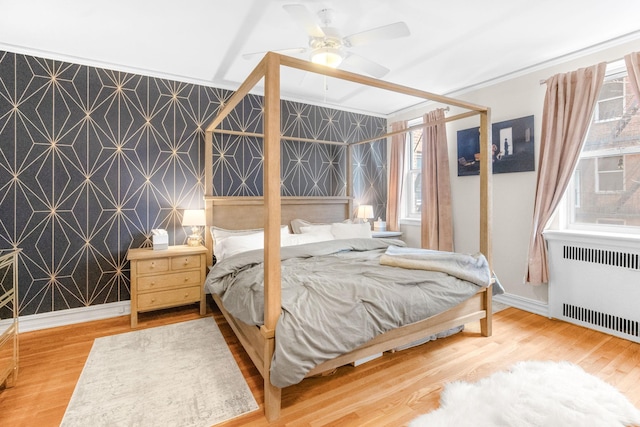 bedroom featuring an accent wall, wood finished floors, radiator heating unit, and wallpapered walls