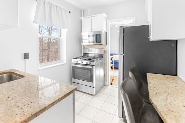 kitchen with light tile patterned floors, white cabinets, appliances with stainless steel finishes, and light stone countertops