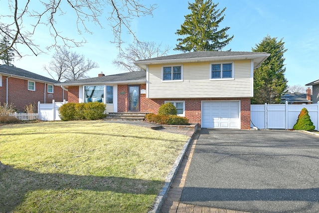 tri-level home featuring fence, driveway, an attached garage, a front lawn, and brick siding