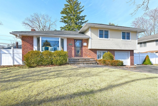 tri-level home featuring brick siding, aphalt driveway, a front lawn, and fence