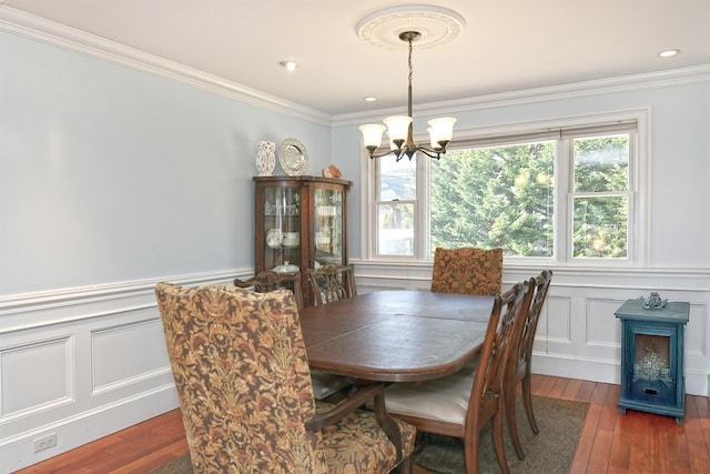 dining space with wood-type flooring, a chandelier, crown molding, and a decorative wall