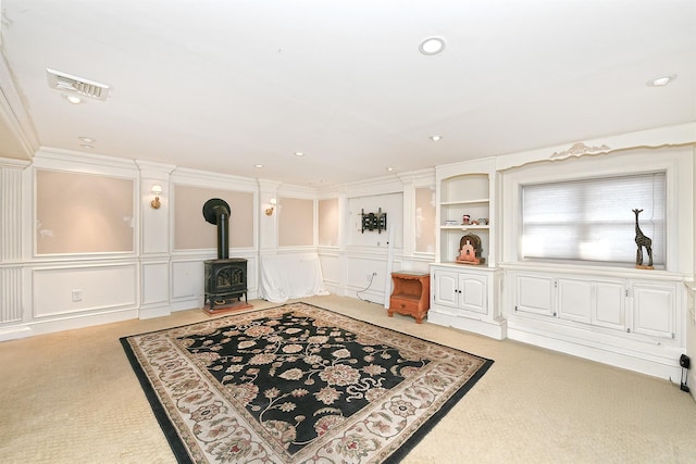 living area featuring visible vents, light colored carpet, a wood stove, and a decorative wall