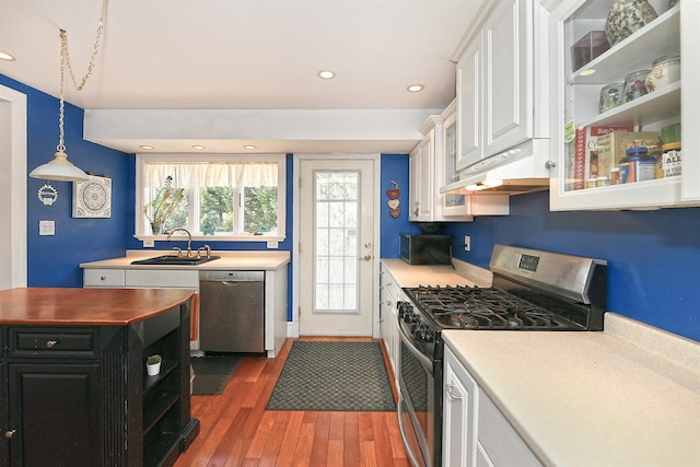 kitchen featuring under cabinet range hood, appliances with stainless steel finishes, wood finished floors, white cabinets, and a sink