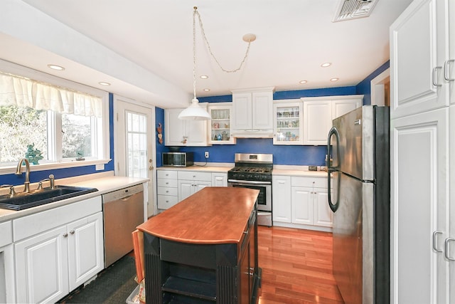 kitchen featuring visible vents, under cabinet range hood, stainless steel appliances, white cabinetry, and a sink