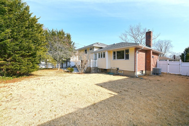 back of house with a gate, central AC, fence, brick siding, and a chimney