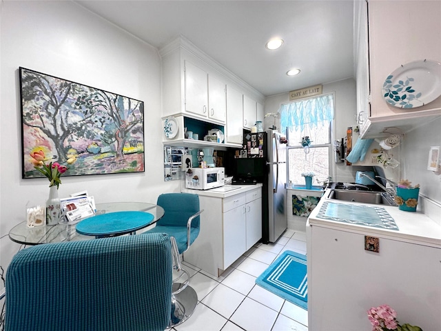 kitchen with light tile patterned floors, white microwave, freestanding refrigerator, a sink, and white cabinetry