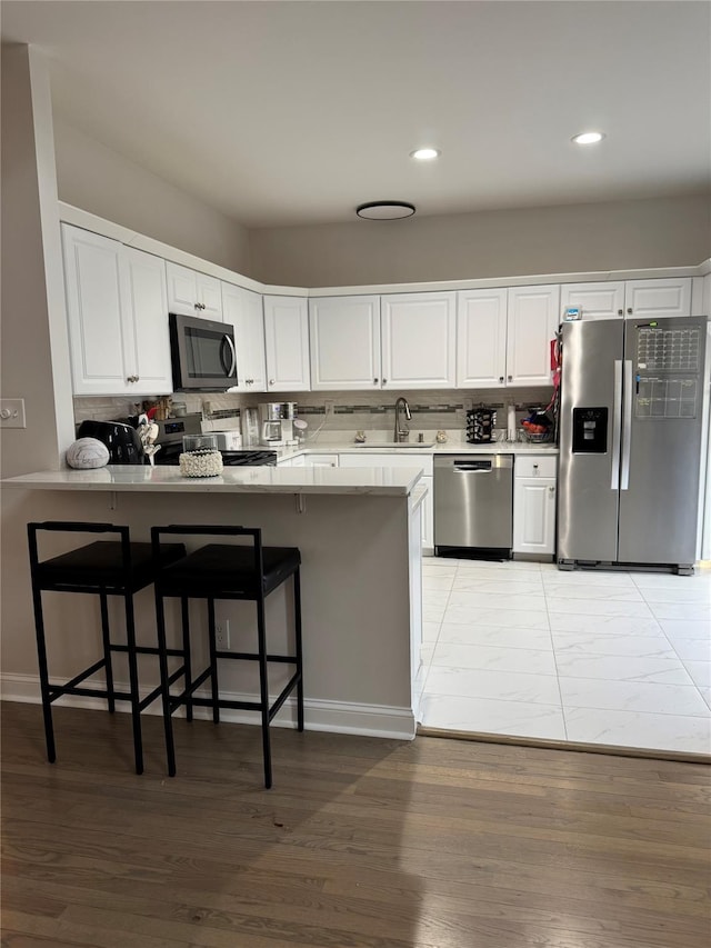 kitchen featuring stainless steel appliances, a peninsula, decorative backsplash, and white cabinetry