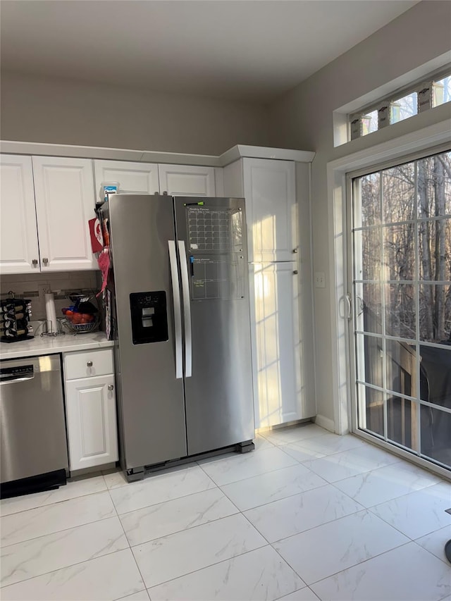 kitchen featuring light countertops, decorative backsplash, appliances with stainless steel finishes, white cabinets, and marble finish floor