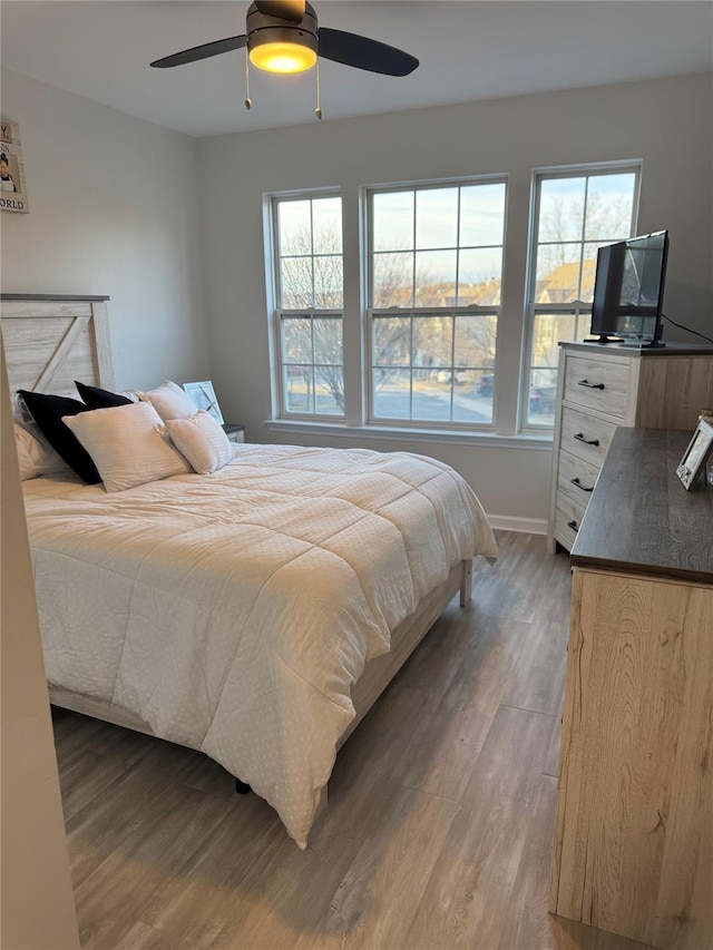 bedroom with multiple windows, a ceiling fan, baseboards, and wood finished floors