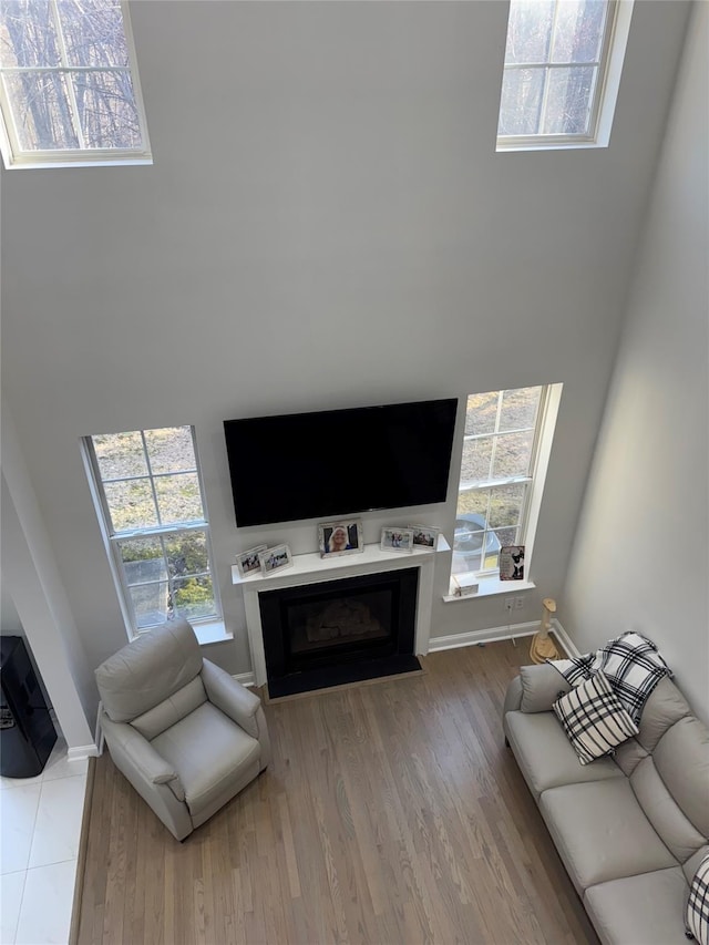 living room featuring baseboards, wood finished floors, a glass covered fireplace, and a towering ceiling