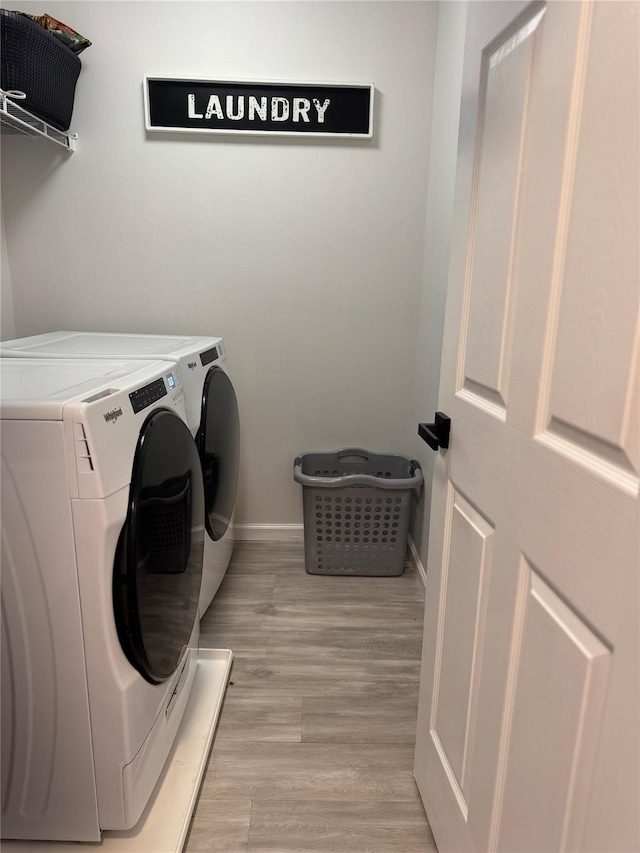 clothes washing area with laundry area, separate washer and dryer, light wood-type flooring, and baseboards