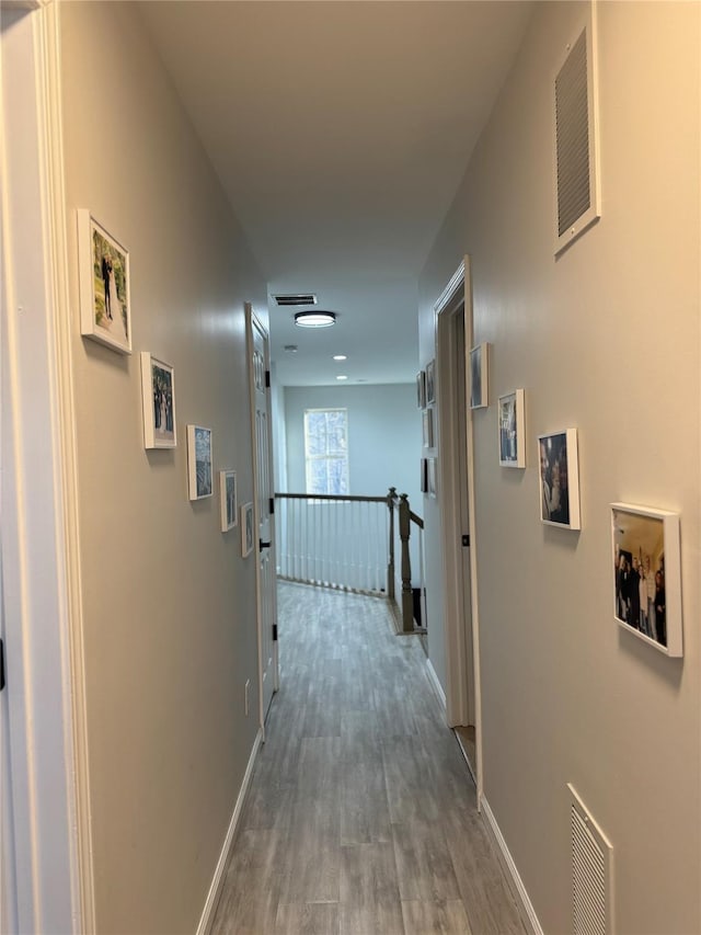 hallway with an upstairs landing, visible vents, baseboards, and wood finished floors