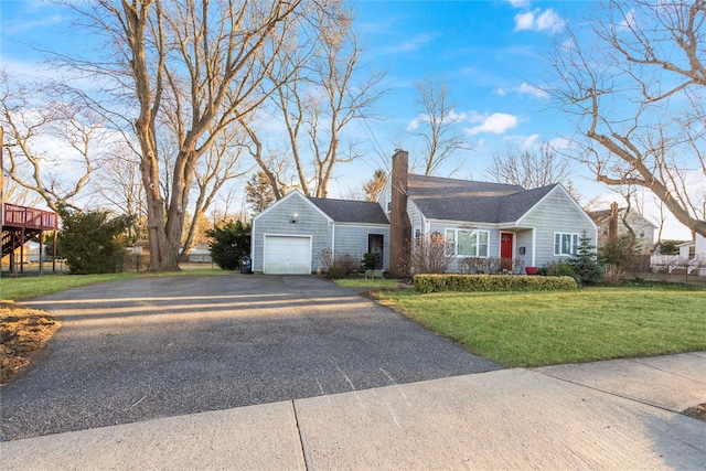 view of front of home featuring a shingled roof, aphalt driveway, a front yard, a chimney, and an attached garage