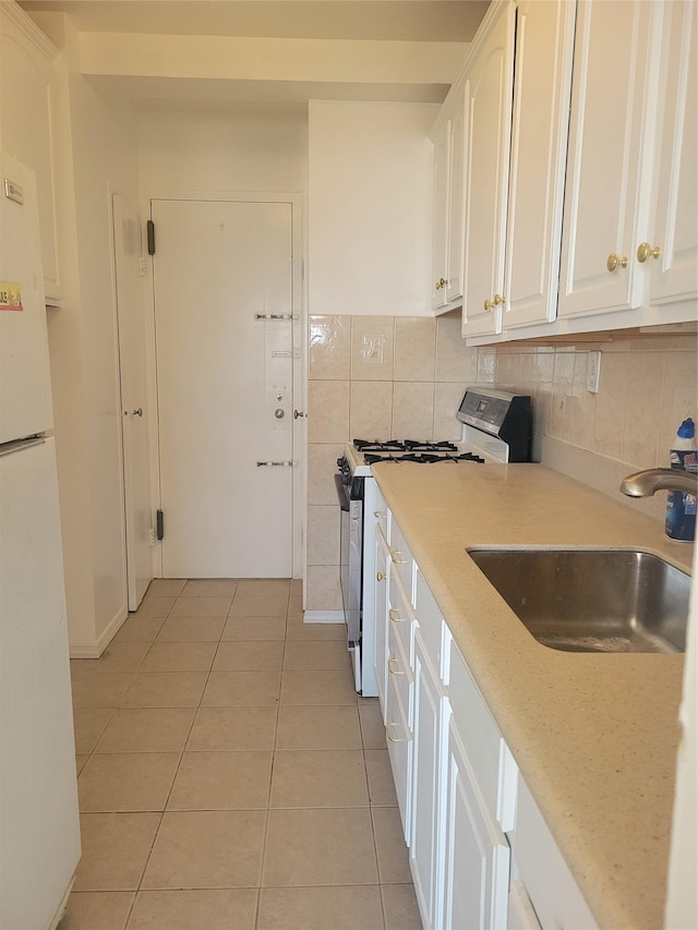 kitchen with a sink, freestanding refrigerator, white cabinetry, gas stove, and light tile patterned floors