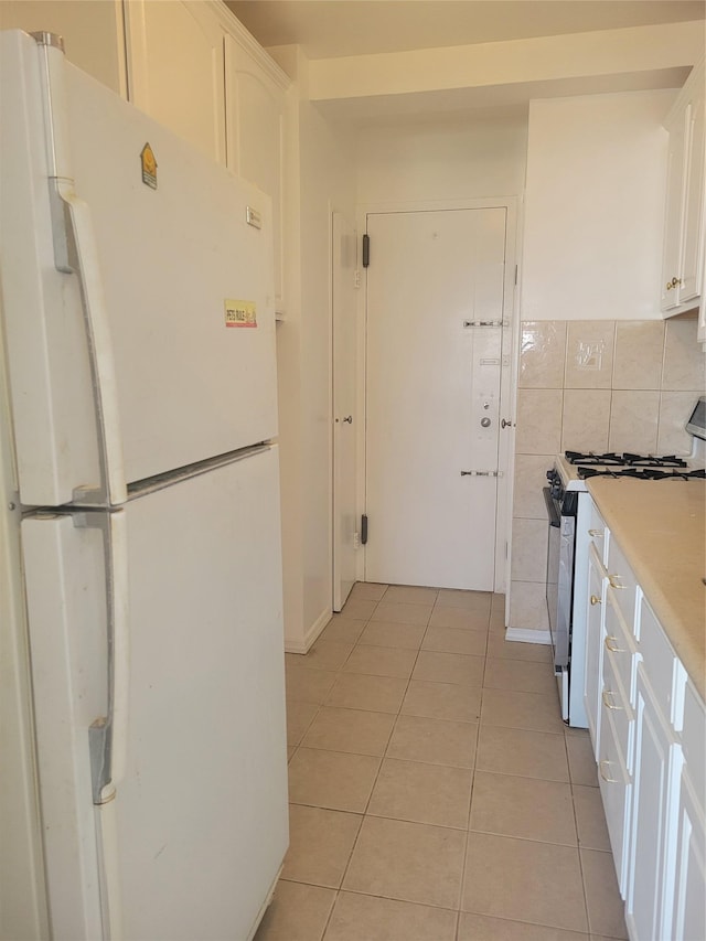 kitchen featuring white cabinets, light tile patterned floors, freestanding refrigerator, light countertops, and stainless steel gas stove