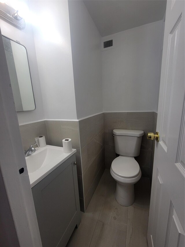 half bath featuring a wainscoted wall, visible vents, toilet, vanity, and tile walls