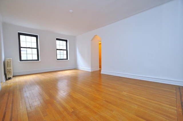 spare room with light wood-type flooring, arched walkways, baseboards, and radiator heating unit