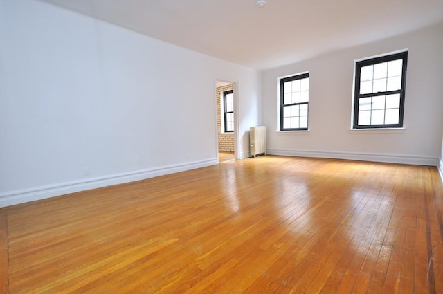 unfurnished room with baseboards, radiator heating unit, and light wood-style floors