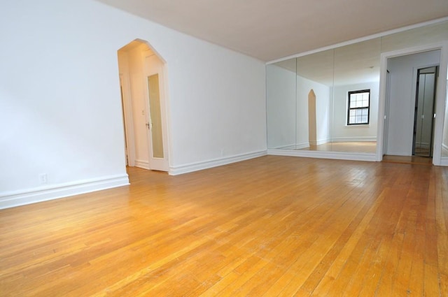 unfurnished room featuring baseboards, arched walkways, and light wood-style flooring