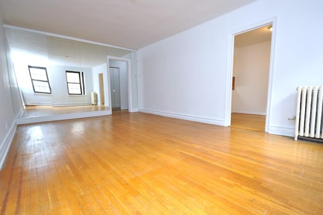 empty room featuring baseboards, radiator heating unit, and light wood-style floors