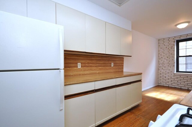 kitchen featuring brick wall, white cabinetry, freestanding refrigerator, and wood finished floors