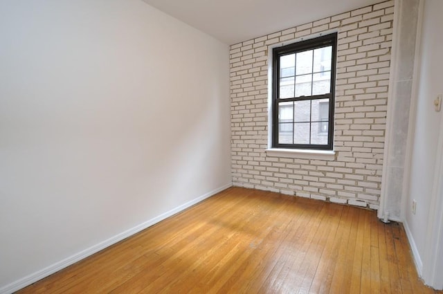 unfurnished room with baseboards, light wood-style flooring, and brick wall