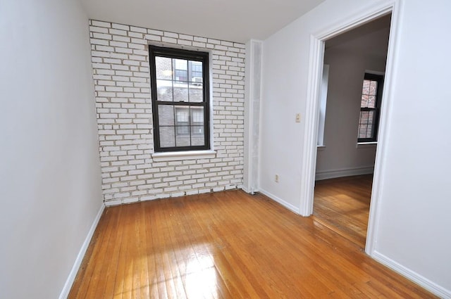 unfurnished room featuring baseboards, wood-type flooring, and brick wall