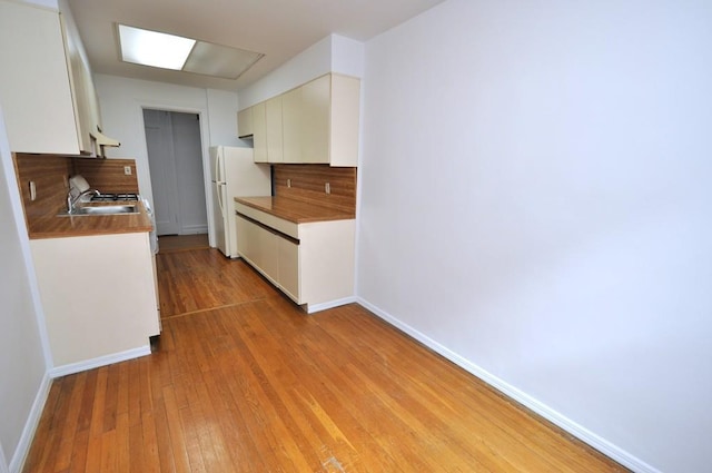 kitchen featuring baseboards, light wood-style flooring, freestanding refrigerator, a sink, and white cabinetry