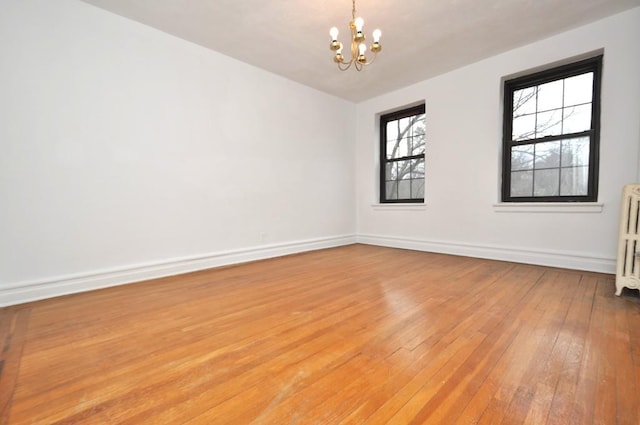 unfurnished room with a notable chandelier, light wood-style flooring, radiator, and baseboards