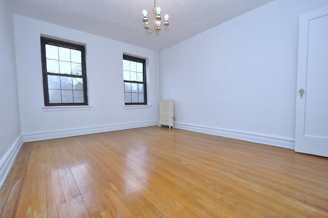 empty room featuring radiator heating unit, baseboards, light wood finished floors, and a chandelier