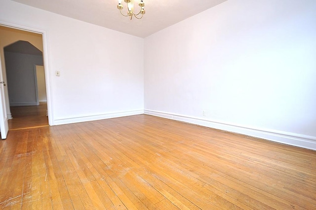 unfurnished room with baseboards, arched walkways, a chandelier, and hardwood / wood-style flooring
