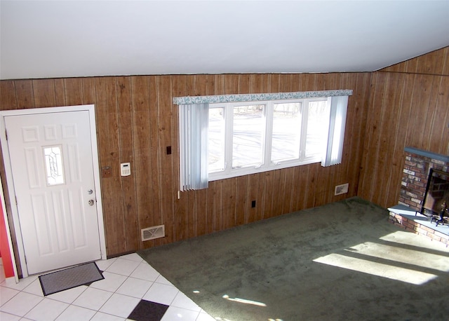 entryway with a brick fireplace, visible vents, and wood walls