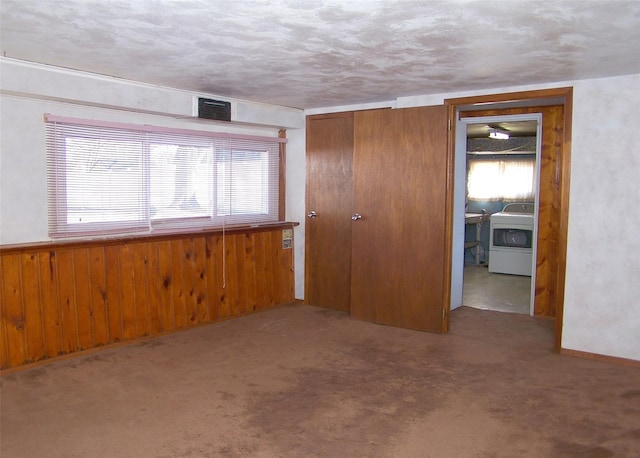 empty room with carpet floors, washer / dryer, wood walls, and a healthy amount of sunlight