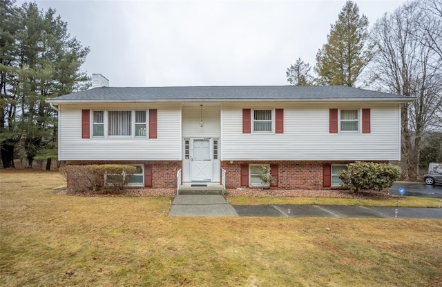 split foyer home with brick siding, a chimney, and a front lawn