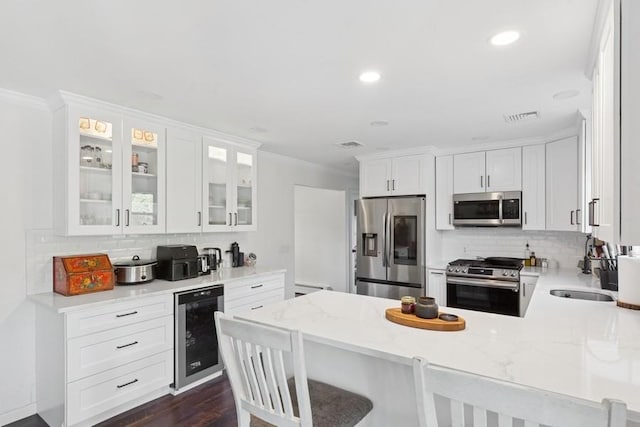 kitchen featuring beverage cooler, a peninsula, a sink, stainless steel appliances, and crown molding