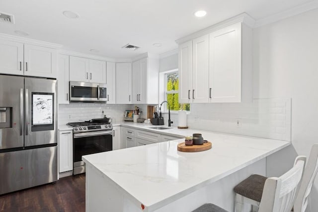 kitchen featuring visible vents, appliances with stainless steel finishes, a peninsula, white cabinets, and a sink