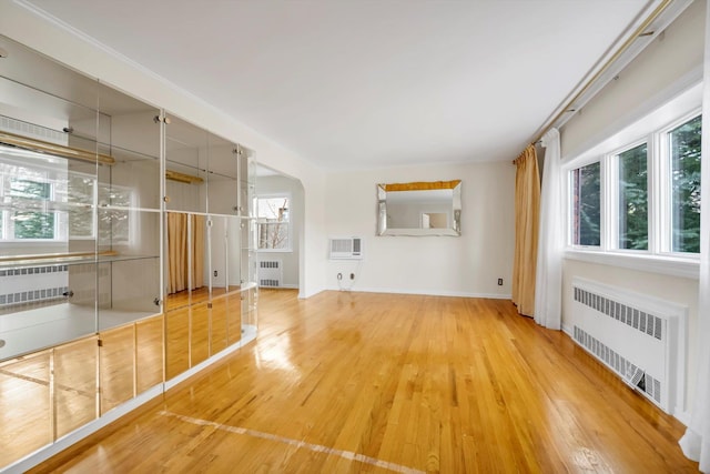 unfurnished living room with radiator heating unit, a wall unit AC, and wood finished floors