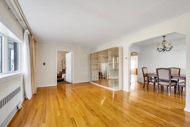 spare room featuring stairs, light wood-style floors, an inviting chandelier, and radiator heating unit